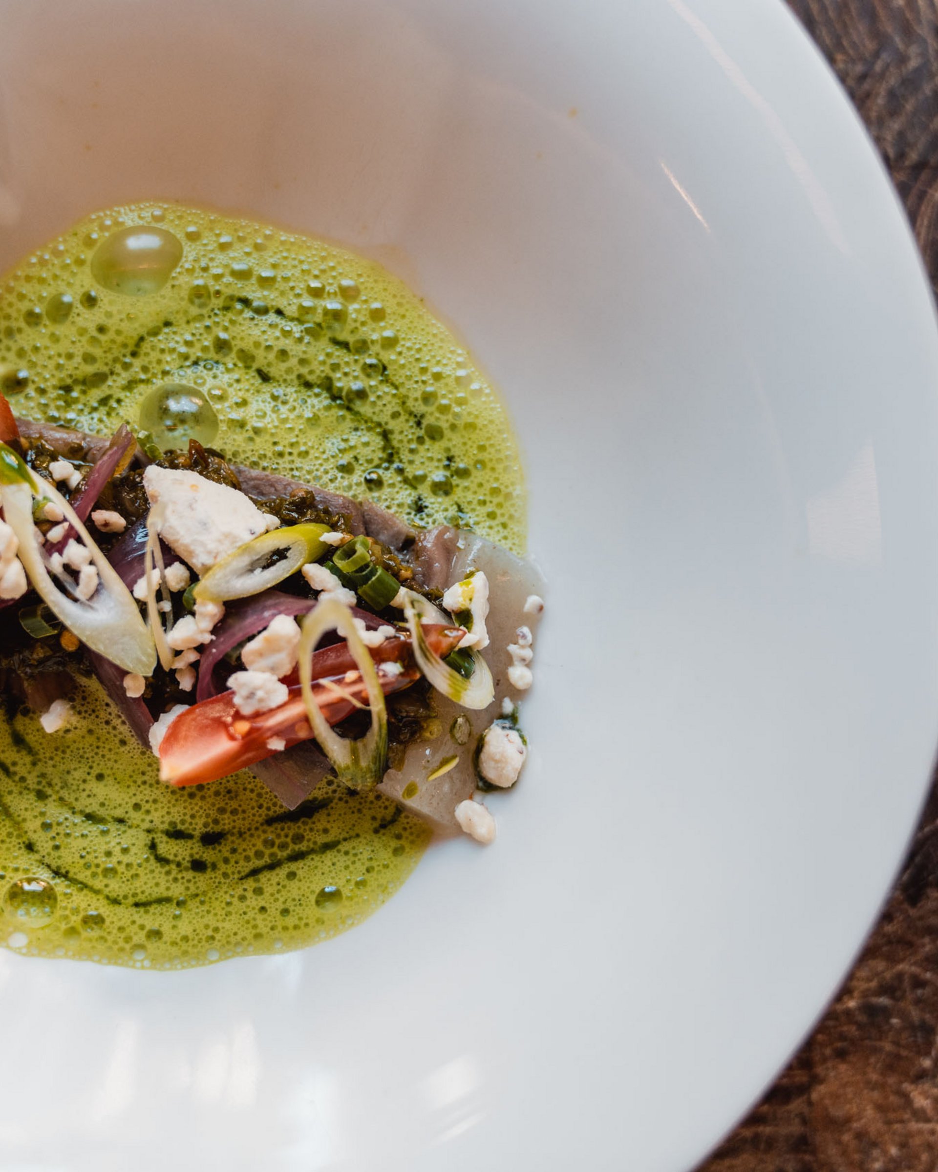 Artfully plated dish with fish, tomatoes, green sauce, and garnish