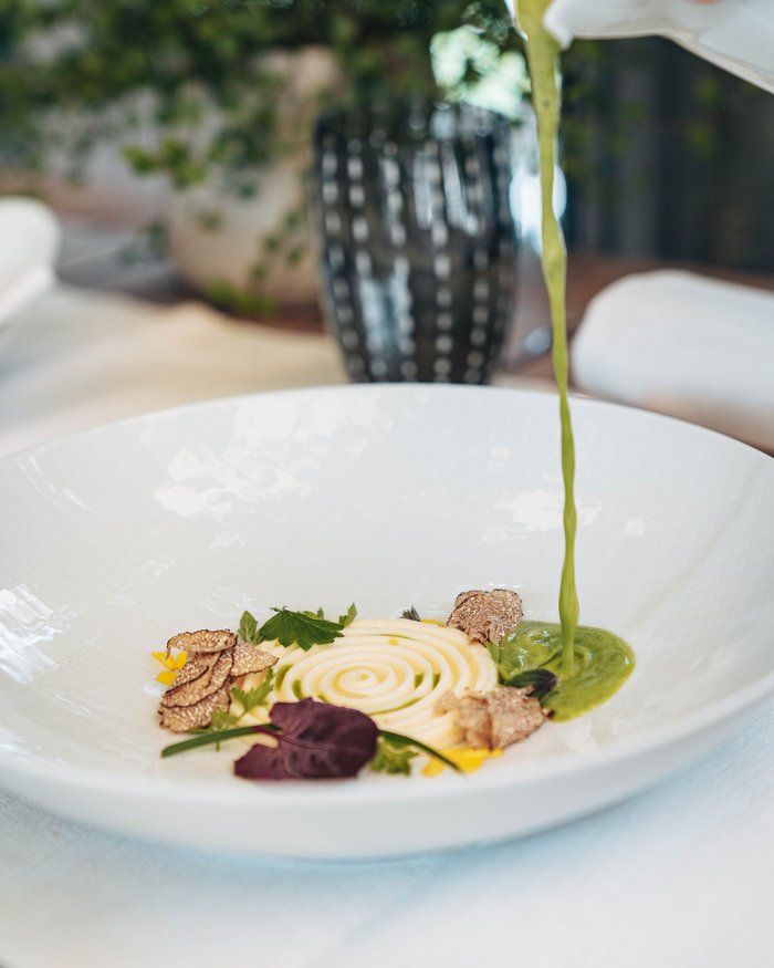 Green sauce poured over an artfully plated dish with mushrooms and herbs