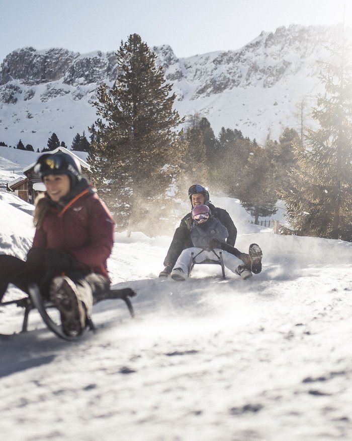 People sledding happily in snow with snowy mountains in background