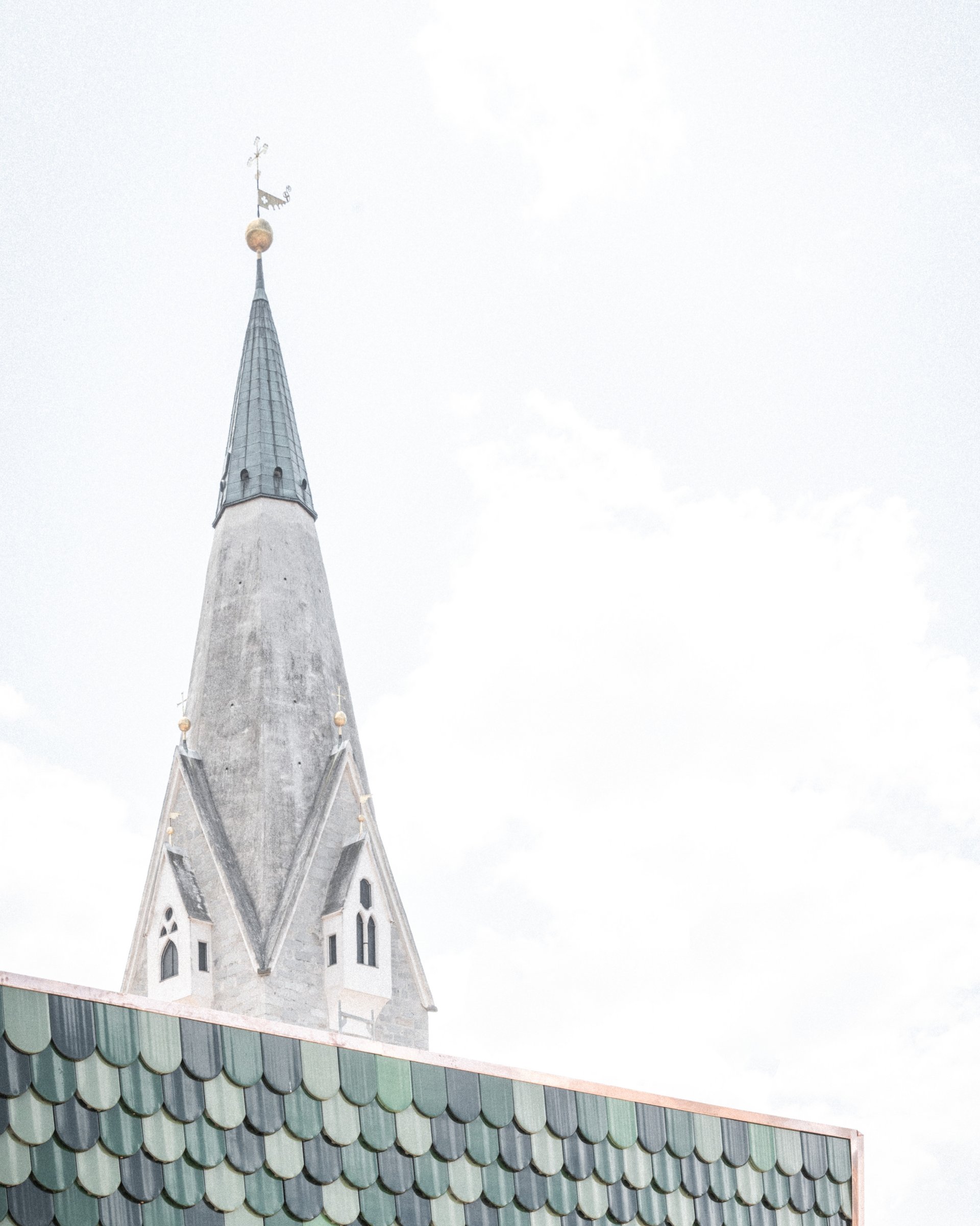Spitzer Kirchturm hinter einem Dach mit grünen Dachziegeln